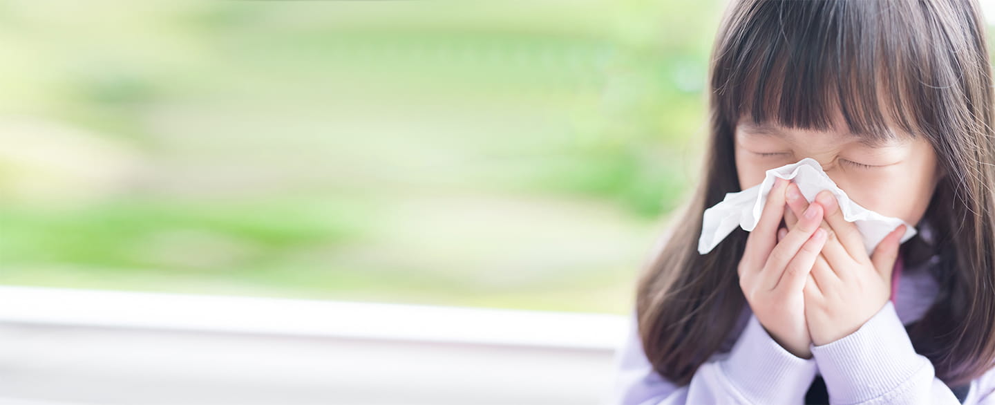 Young girl sneezing into a tissue.