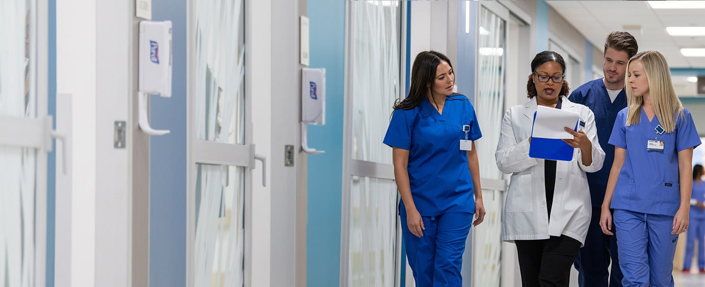 Physician consulting with nurses in hospital hallway.